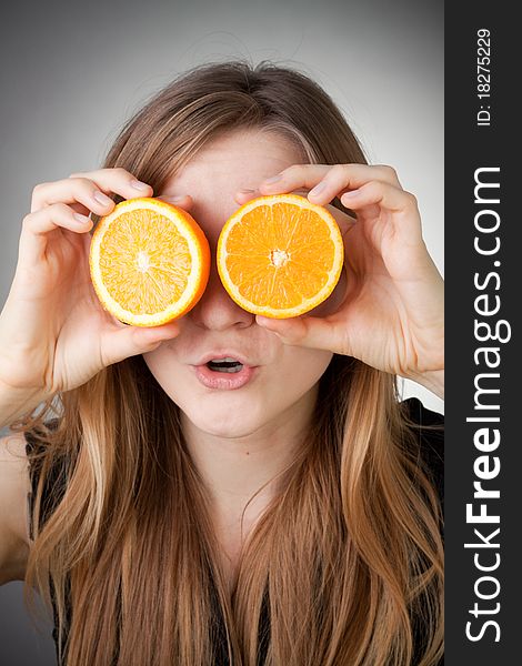 Beautiful blond girl using orange as glasses, with grey background