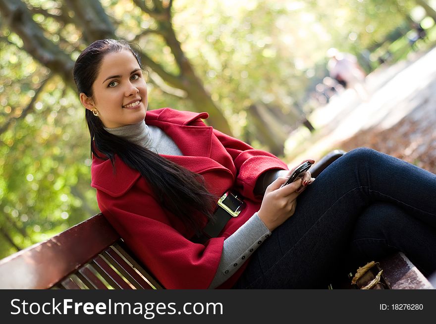 Young Caucasian woman with a cell phone, sitting in a park on a wooden bench, reading a SMS. Young Caucasian woman with a cell phone, sitting in a park on a wooden bench, reading a SMS.