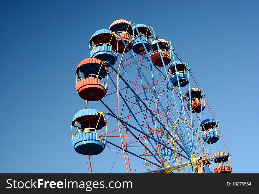 Low angle view of ferris wheel with colorful gondolas and blue sky background. Low angle view of ferris wheel with colorful gondolas and blue sky background.