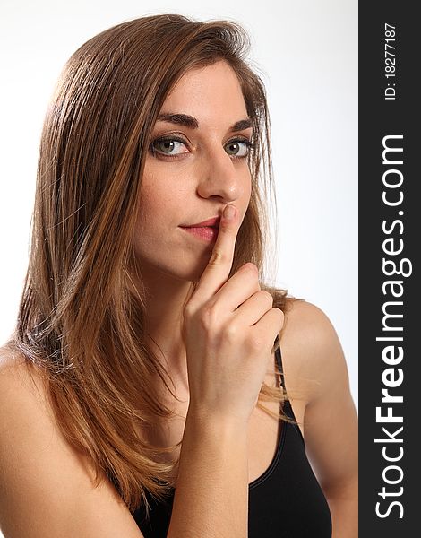 Headshot of beautiful young woman, finger over her lips, indicating quiet, or keep it secret. Model has serious expression on her face looking straight to camera. Headshot of beautiful young woman, finger over her lips, indicating quiet, or keep it secret. Model has serious expression on her face looking straight to camera.