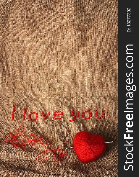 Cross stich 'I love you' with knit ball in a form of a heart pierced with needle. Cross stich 'I love you' with knit ball in a form of a heart pierced with needle
