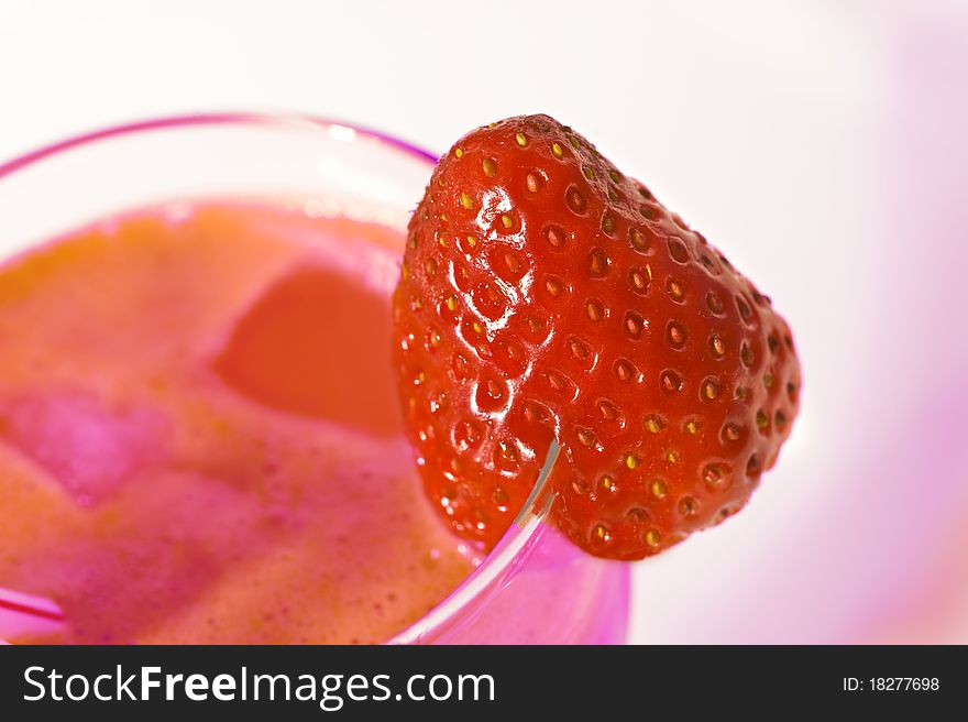 A fresh strawberry on the rim of a glass of multi colored juice. A fresh strawberry on the rim of a glass of multi colored juice