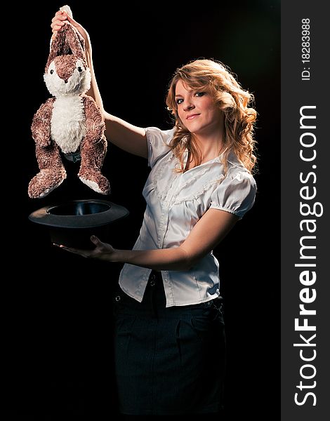 Pretty young grey-eyed blondie getting a toy rabbit out of the hat. Black background, ready for isolation. Pretty young grey-eyed blondie getting a toy rabbit out of the hat. Black background, ready for isolation