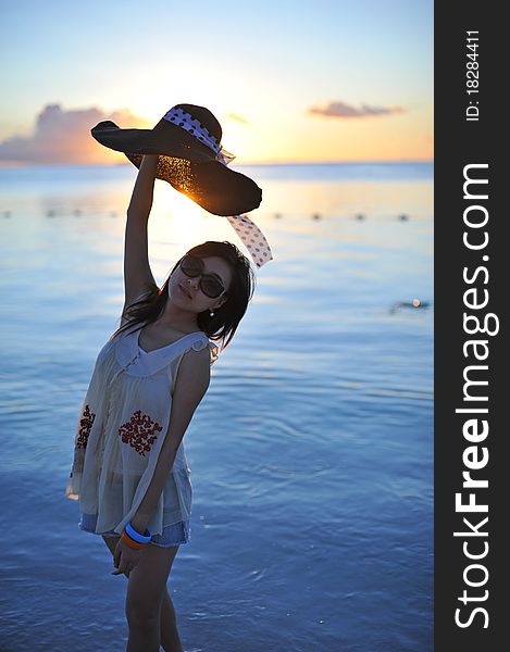 Girl on the beach of Saipan Island with the beautiful sunset.She put the straw hat in the air to cover the shining sun. Girl on the beach of Saipan Island with the beautiful sunset.She put the straw hat in the air to cover the shining sun.
