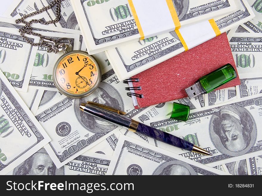 Pocket watch, notebook and pen on a stack of dollars, reflecting time and money