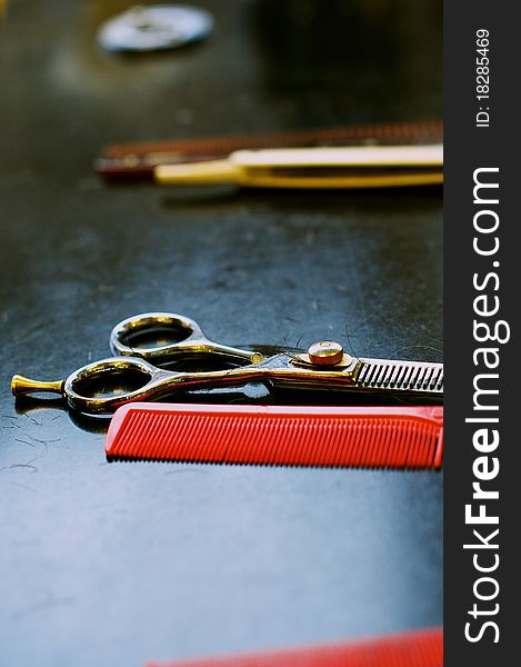 Barbers' thinning scissors with red comb on black work surface with white cut throat in background. Barbers' thinning scissors with red comb on black work surface with white cut throat in background