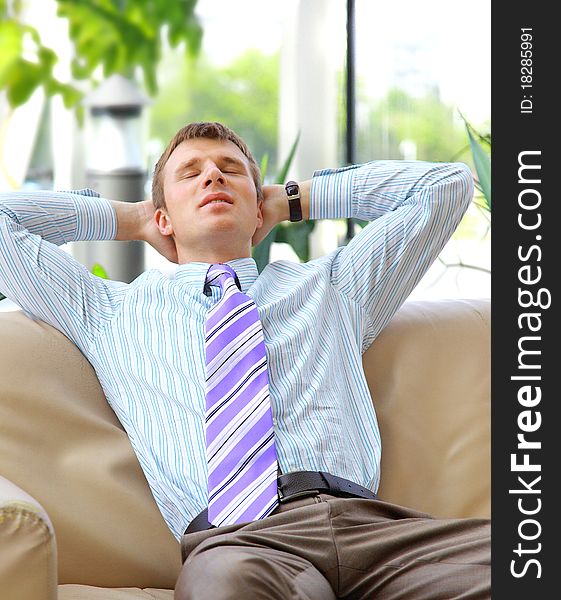 Young relaxed business man with hands behind head at work