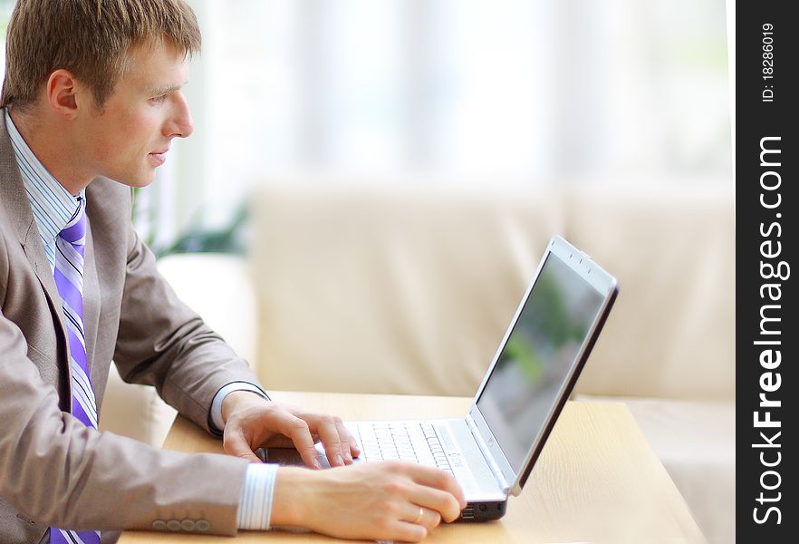 Businessman sitting at desk in office, working with laptop computer, looking back, smiling