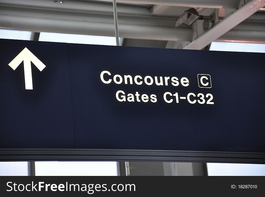 A dark blue airport sign reading Concourse C and Gates C1 to C32 in white with a directional arrow. A dark blue airport sign reading Concourse C and Gates C1 to C32 in white with a directional arrow