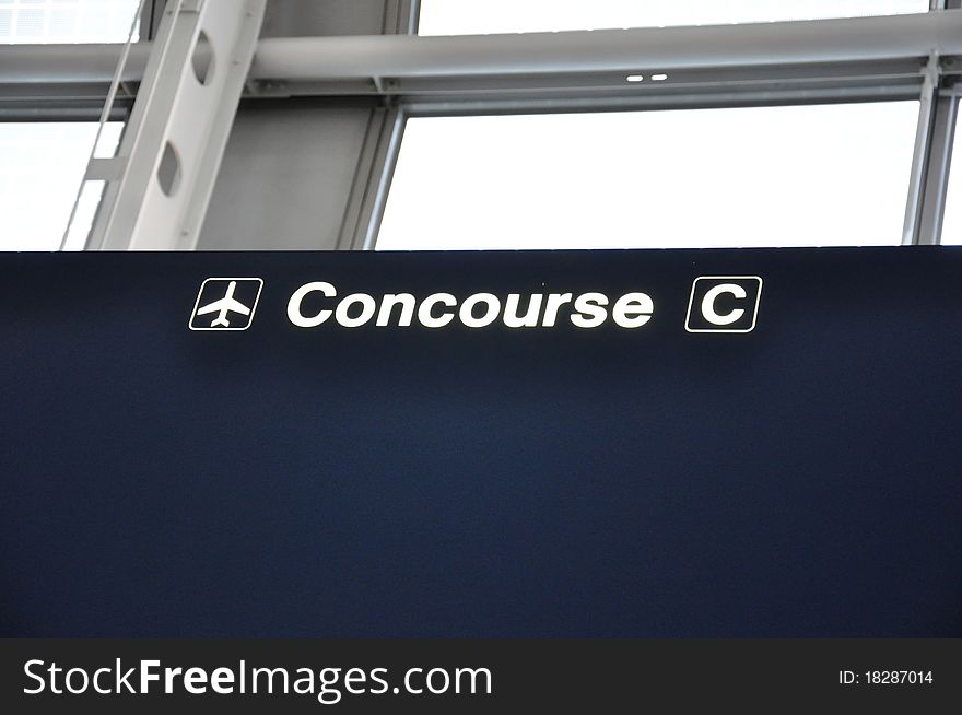 A dark blue airport sign reading Concourse C with a directional arrow in white. A dark blue airport sign reading Concourse C with a directional arrow in white