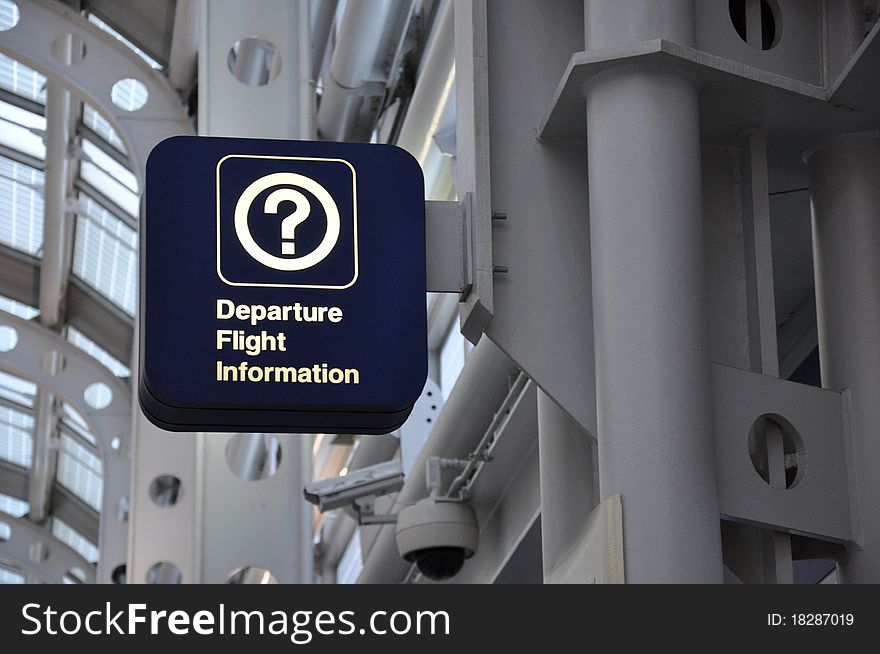 A dark blue sign reading Departure Flight Information with a question mark symbol against a gray industrial background
