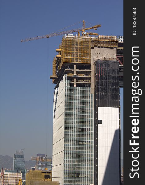 Office tower under construction, covered in a network of metal scaffolding and large yellow construction crane towering above. Clear blue sky behind. Office tower under construction, covered in a network of metal scaffolding and large yellow construction crane towering above. Clear blue sky behind.