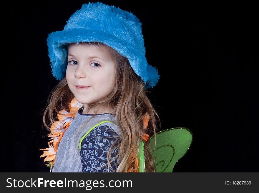 A little girl in with small smile dressed up in blue hat, lei and fairy wings. A little girl in with small smile dressed up in blue hat, lei and fairy wings