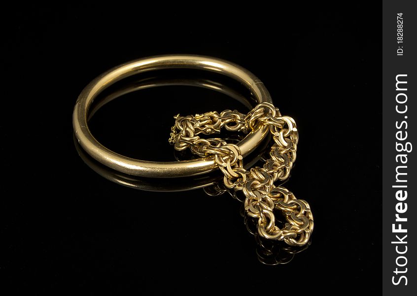Close-up of two gold bracelets with reflex on black background
