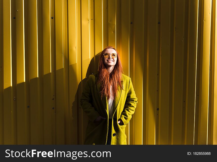 Happy red hair girl standing against yellow wall and looking up. Copy space