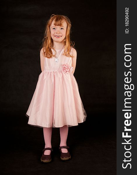 Cute little girl in pink dress against black background