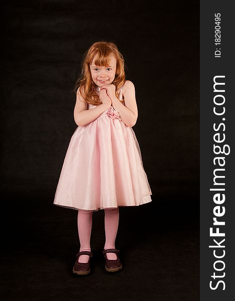 Cute little girl in pink dress against black background
