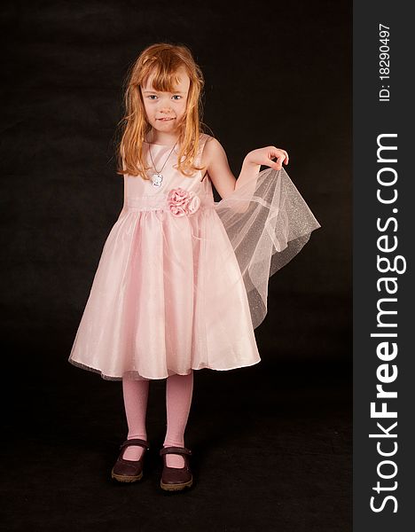 Cute little girl in pink dress against black background