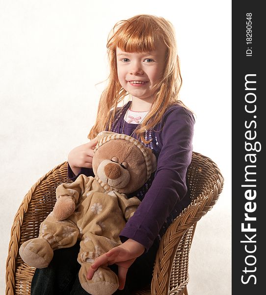 Cute little girl sitting in a chair holding a teddy bear