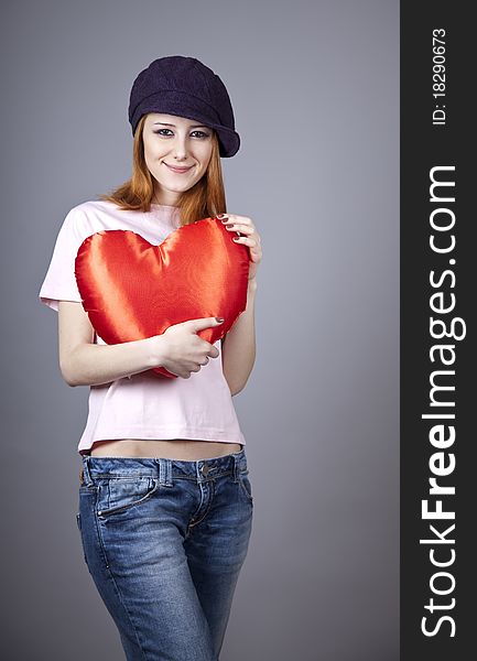 Beautiful red-haired girl in cap with toy heart. Studio shot.