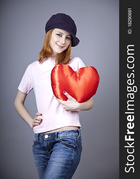 Beautiful red-haired girl in cap with toy heart. Studio shot.