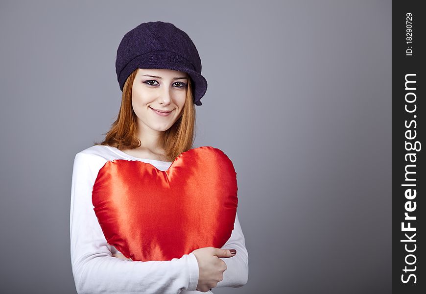 Beautiful red-haired girl in cap with toy heart. Studio shot.