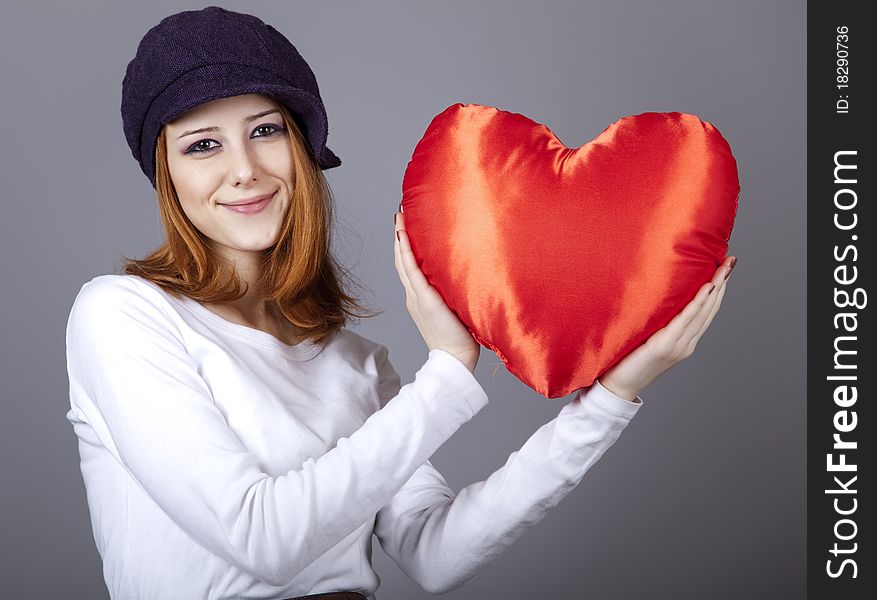 Beautiful red-haired girl in cap with toy heart. Studio shot.