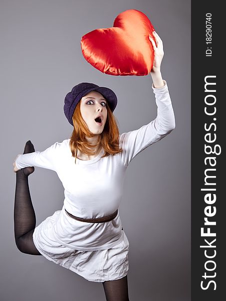 Beautiful red-haired girl in cap with toy heart. Studio shot.