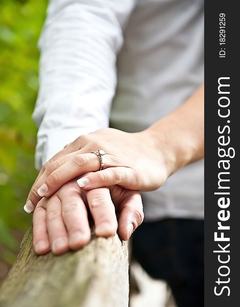 A couple holding hands on a fence with an engagement ring visible. A couple holding hands on a fence with an engagement ring visible