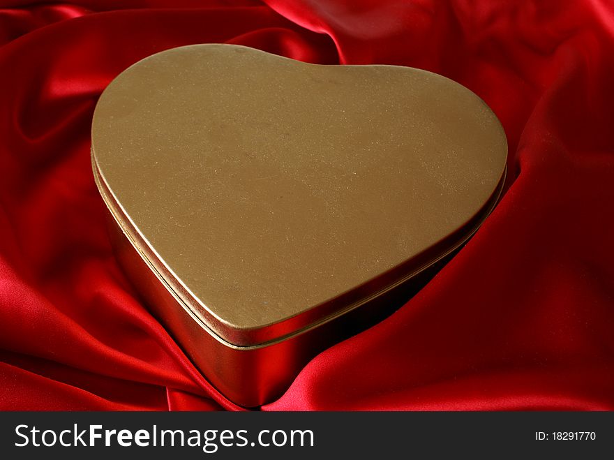 A golden heart shaped container on top of some red satin.