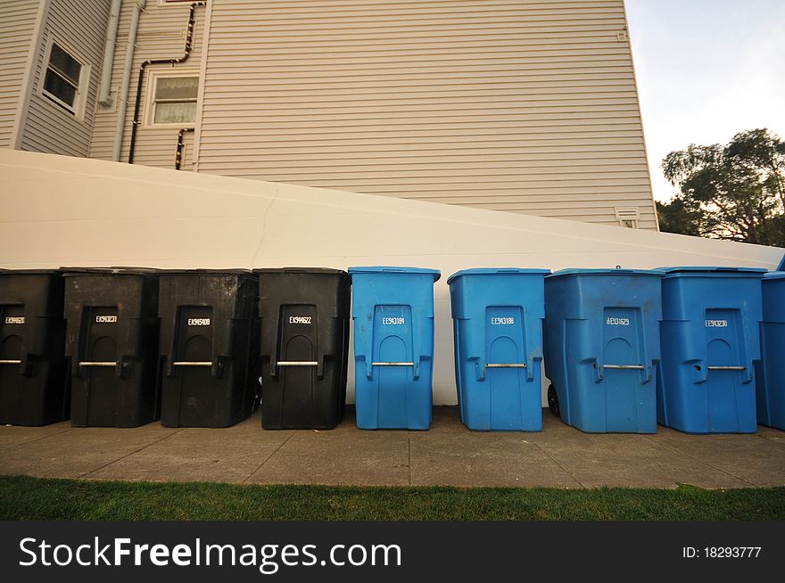 A row of recycling and garbage cans next to a wall. A row of recycling and garbage cans next to a wall