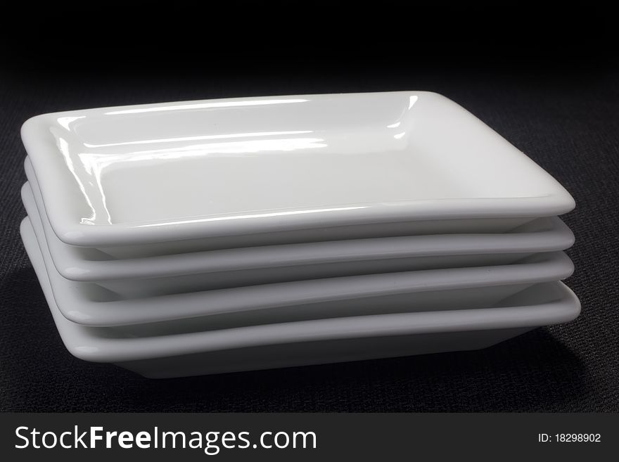 White square ceramic plates for dessert dishes on a black background. White square ceramic plates for dessert dishes on a black background.