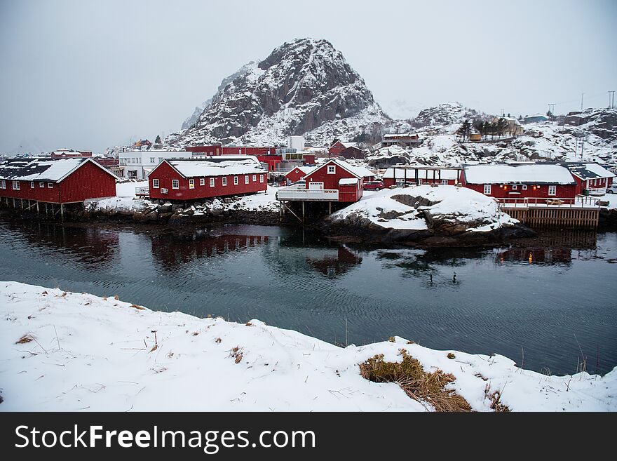 Red fishing house rorbu near cold blue fjord at snowy winter time. Snowy mountains pick on background. Lofonet islands
