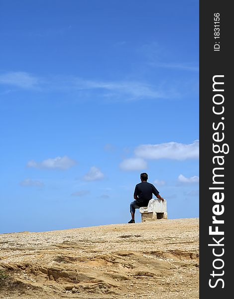 Man sitting on a bench with blue cloudy sky