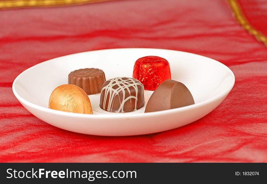 Plate with chocolates on a red stuff background