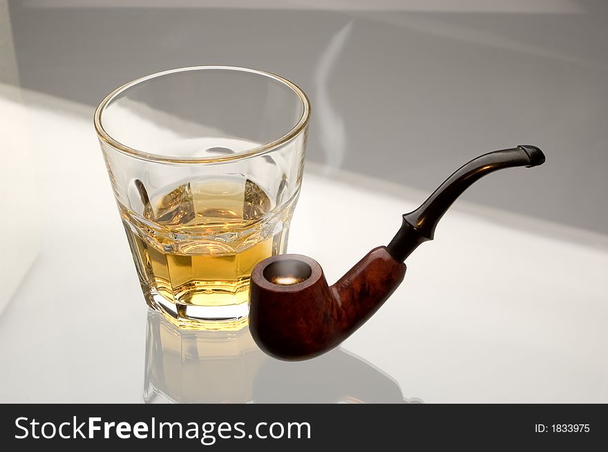 Glass of whiskey and pipe on glass close up