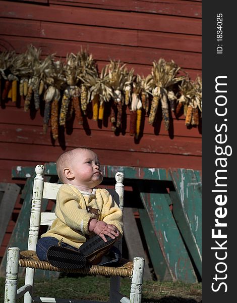 Image of baby boy sitting on a chair in front of a red farm building. Image of baby boy sitting on a chair in front of a red farm building