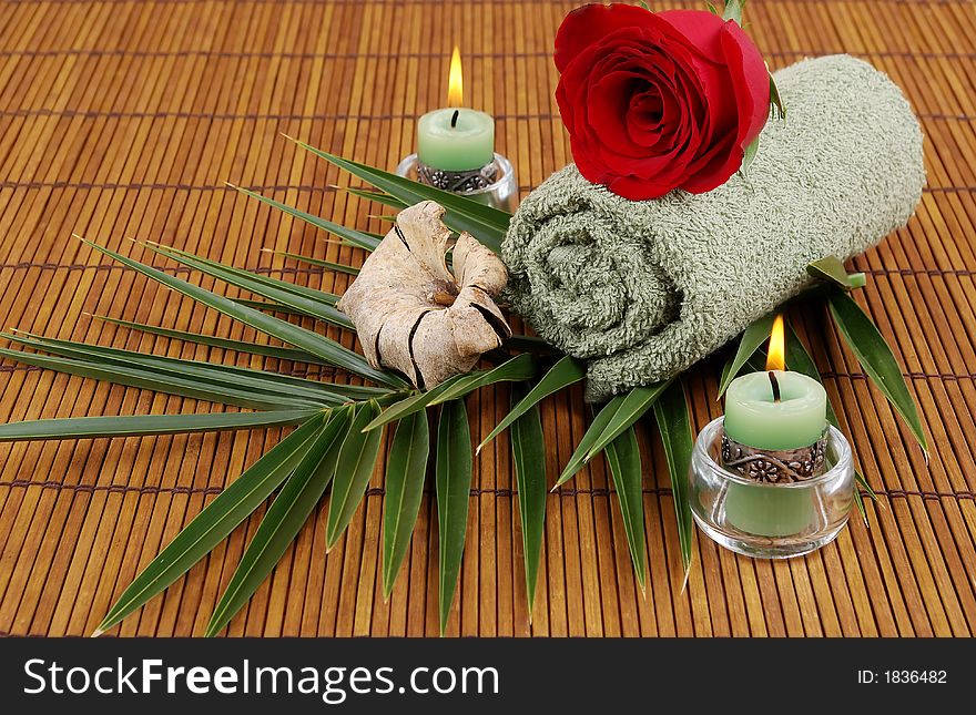 Rose, palm frond, towel, and candles on bamboo