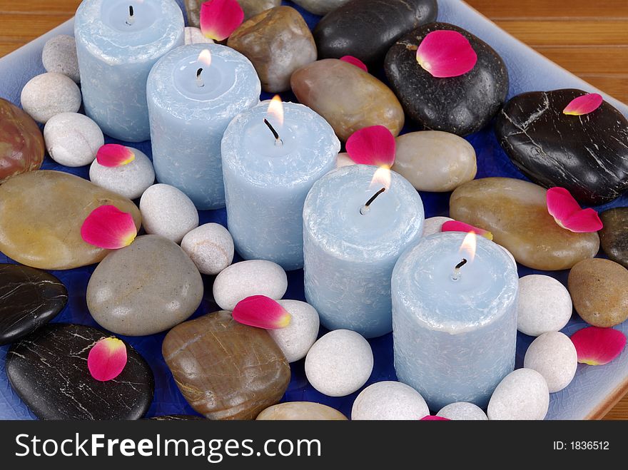 Blue candles and rose petals on pebbles