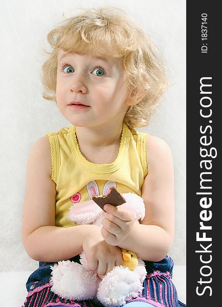 Little blonde curly girl eating chocolate with toy