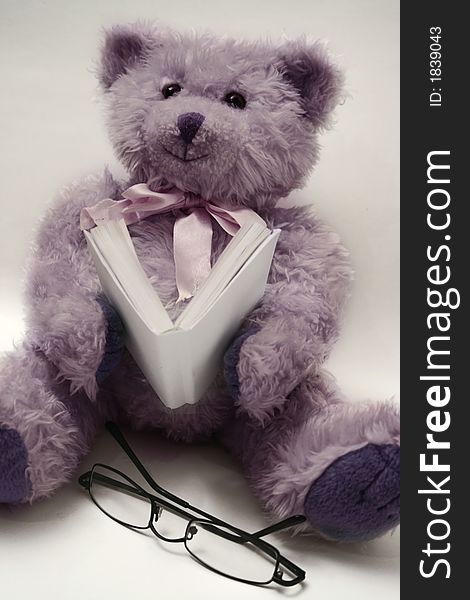 Sitting and reading teddy bear looking at the camera and with glasses near