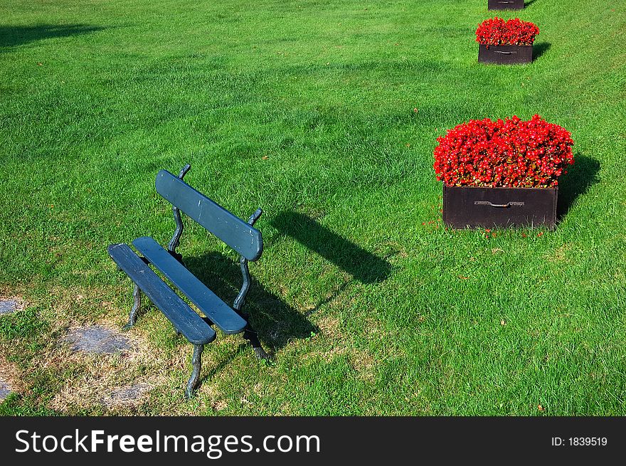 Park Bench on a sunny day, with red flowers vases