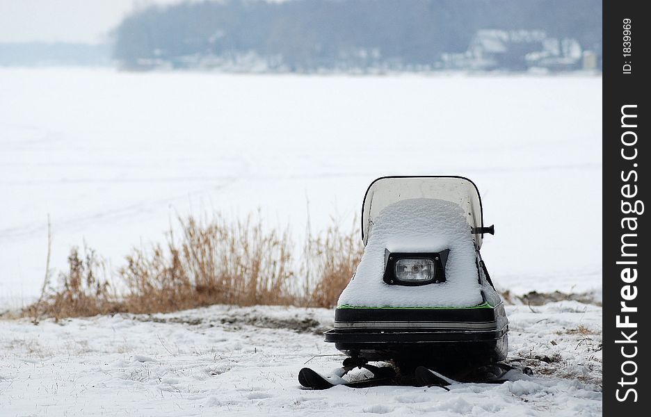 A snow covered child's snowmobile sitting side of frozen lake. A snow covered child's snowmobile sitting side of frozen lake.