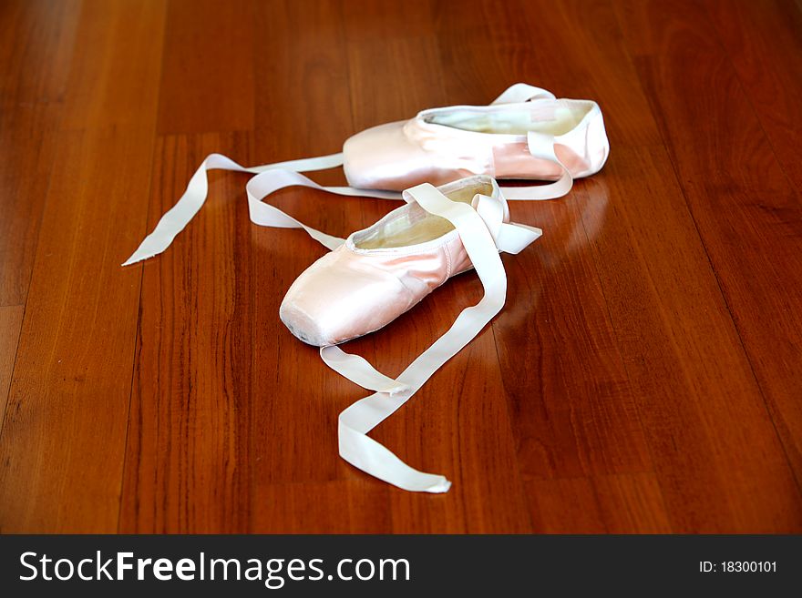 Ballet pointe shoes of pink satin on the wooden studio floor.