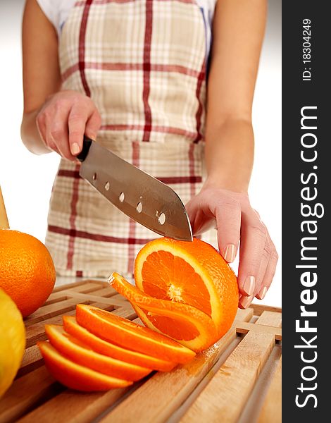 Girl cutting orange with the knife, on a wooden plate