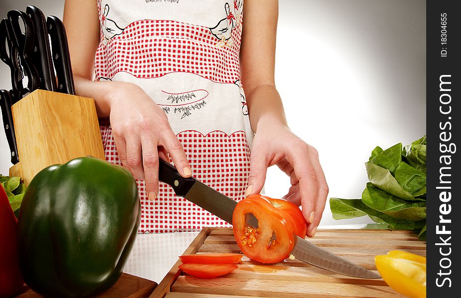 Girl cutting tomato with the knife, on a wooden plate. Girl cutting tomato with the knife, on a wooden plate