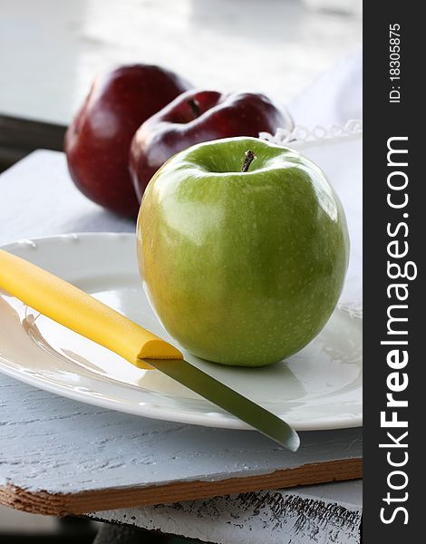 Granny Smith apple on white plate; two Red Delicious apples in background.