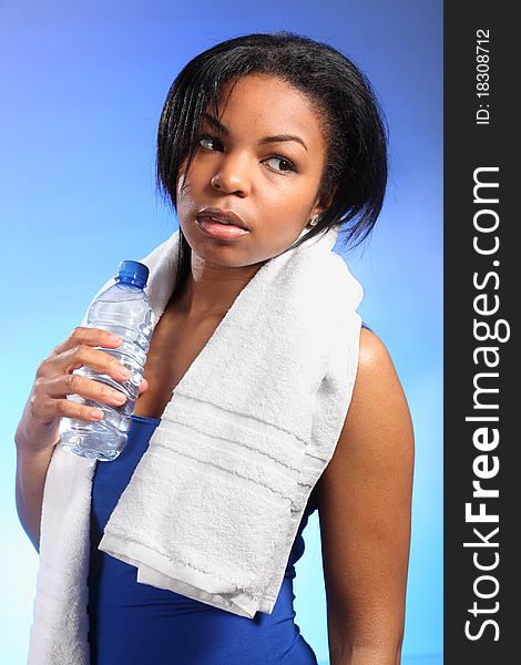 Portrait of beautiful black woman, looking tired after working out. She is wearing a blue vest, has a white towel around her shoulders and holding a bottle of water. Portrait of beautiful black woman, looking tired after working out. She is wearing a blue vest, has a white towel around her shoulders and holding a bottle of water.