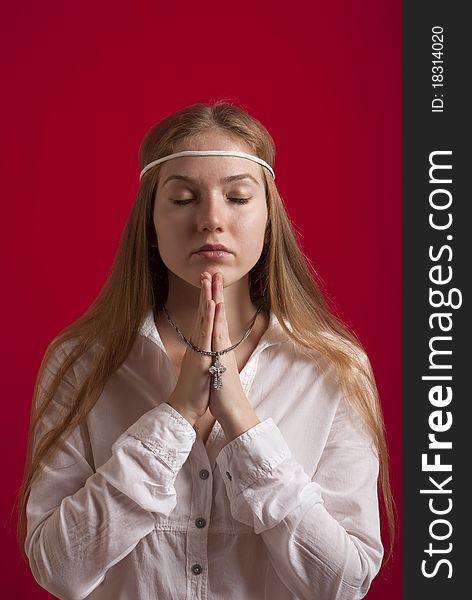 Young woman in a white shirt with a cross on a silver chain  praying. On red background. Young woman in a white shirt with a cross on a silver chain  praying. On red background.