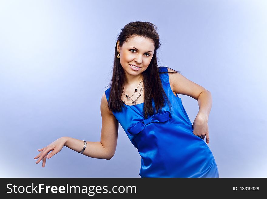 Beautiful fashion cheery girl pointing in a bright-blue dress on a light-blue background. Beautiful fashion cheery girl pointing in a bright-blue dress on a light-blue background